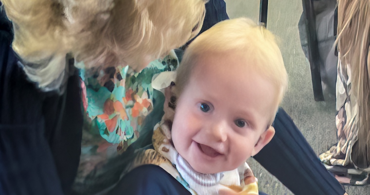 A toddler sitting in a grandparents lap, playing on the floor in a group setting.